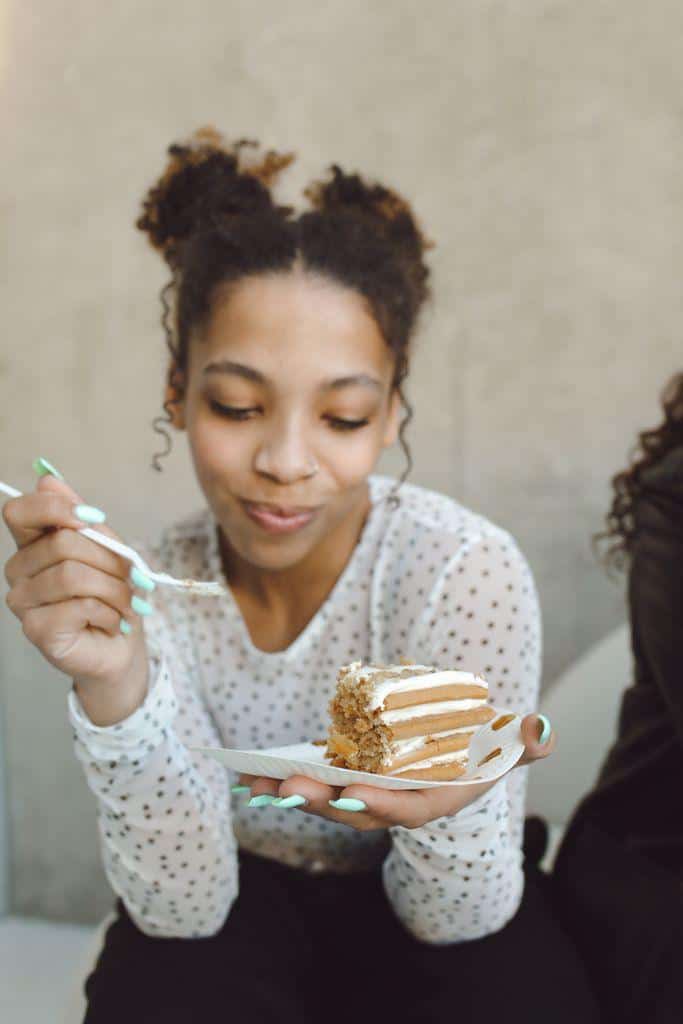 A cheerful young woman enjoys a slice of cake indoors, savoring a delightful moment.