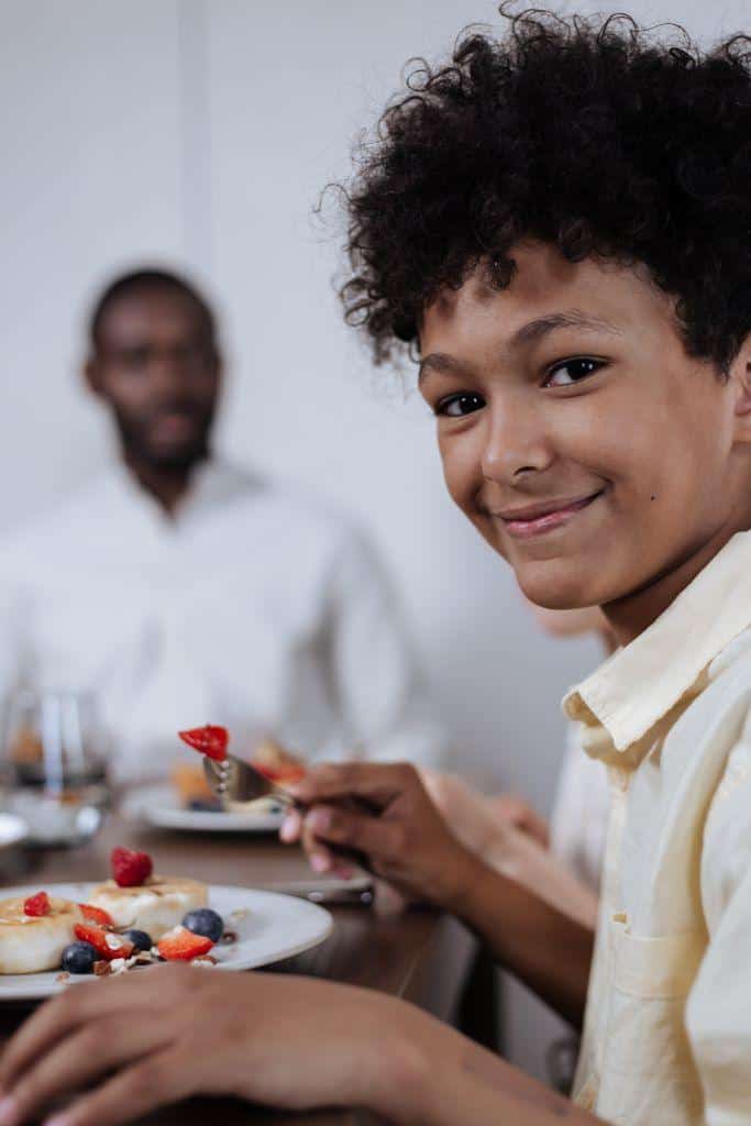 A joyful moment at the breakfast table with a smiling boy and family enjoying pancakes and berries.
