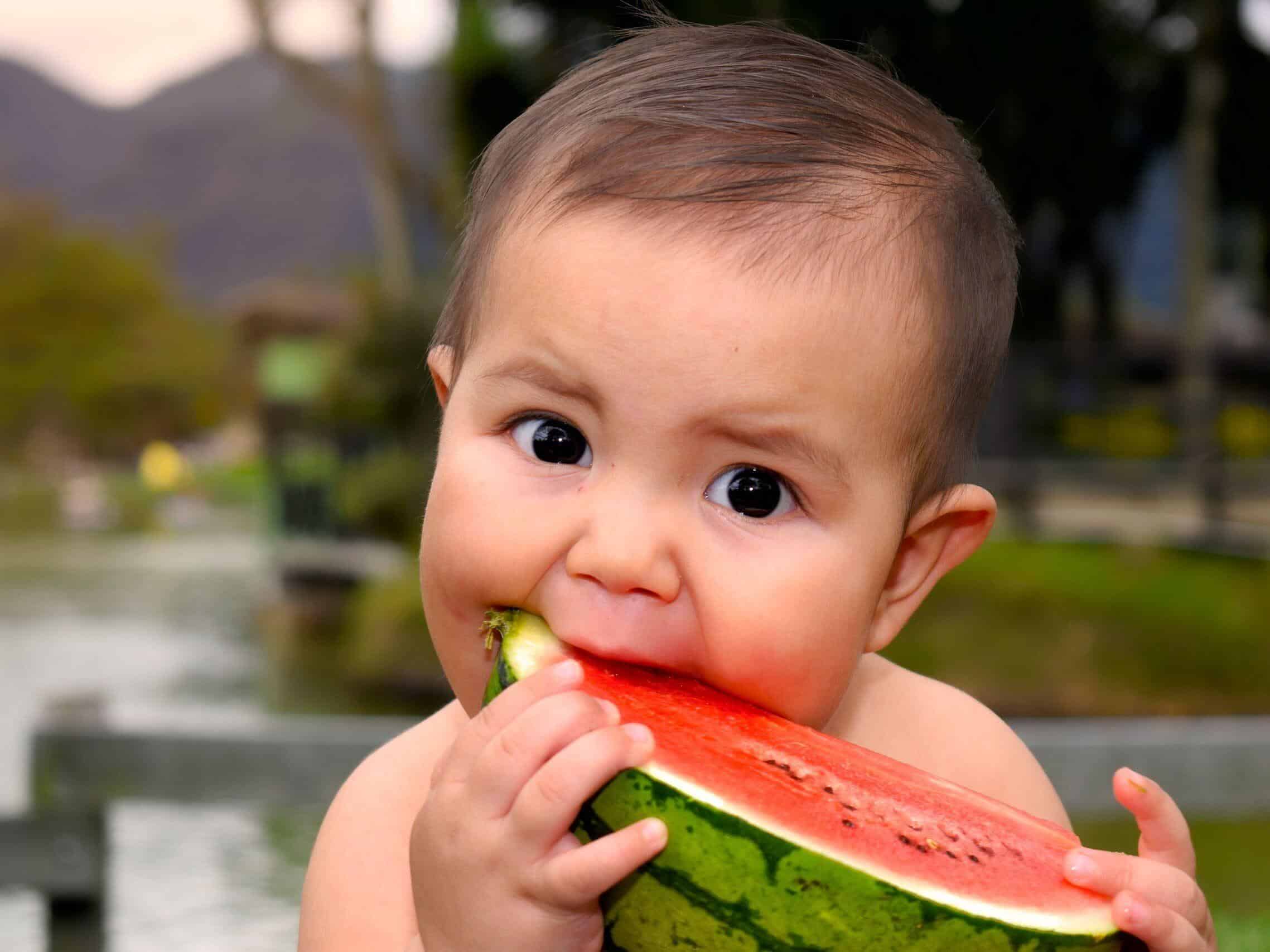 Cute baby eating a juicy watermelon slice outdoors in a park setting.
