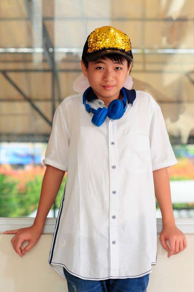 Portrait of a smiling Asian boy in a white shirt with colorful headphones and a sequin cap.